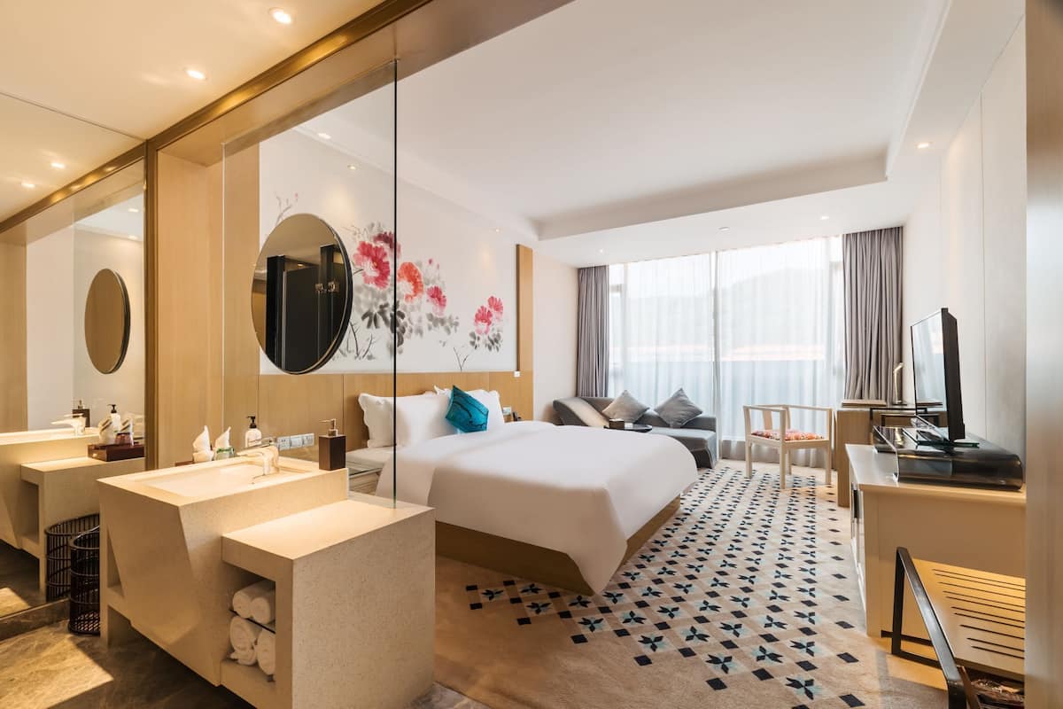 Et moderne hotelværelse med en stor seng, et skrivebord, et toiletbord med spejl og et stort vindue.