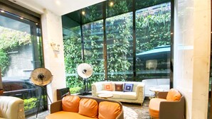 A modern lounge area with a sofa, armchairs, a fan, and large windows offering a view of greenery. - Paco Hotel Taojin Metro Guangzhou (Guangzhou)