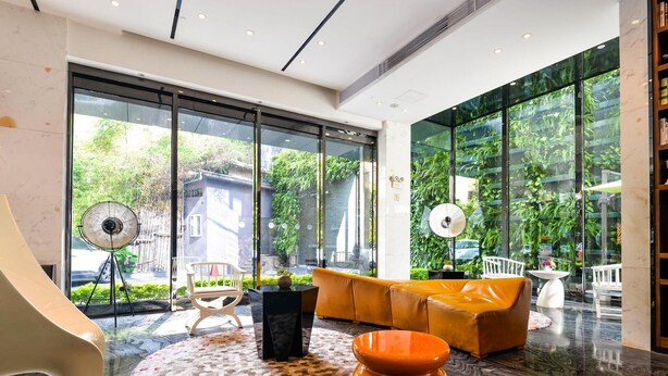 A modern interior with a sofa, a unique orange chair, a black table, and a large window with a view of greenery. - Paco Hotel Taojin Metro Guangzhou (Guangzhou)