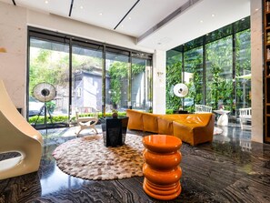 A modern interior with a sofa, a unique orange chair, a black table, and a large window with a view of greenery. - Paco Hotel Taojin Metro Guangzhou (Guangzhou)