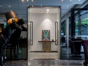 Un interior moderno con puerta de entrada de vidrio, una escultura de un caballo y una obra de arte minimalista sobre una consola.