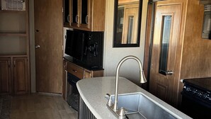 Eine Küche mit einer Granitarbeitsplatte, einer Edelstahl-Spüle, Holzschränken, einer Mikrowelle und einem Deckenventilator.