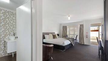 Ein Hotelzimmer mit Bett, Schreibtisch, Stuhl, Badezimmer mit Waschbecken und einem Fenster mit Vorhängen.