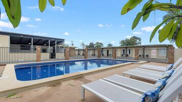 A swimming pool with lounge chairs, a covered area, and a brick building in the background.