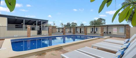 A swimming pool with lounge chairs, a covered area, and a brick building in the background.