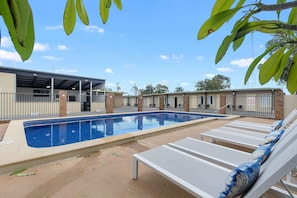 A swimming pool with lounge chairs, a covered area, and a brick building in the background.
