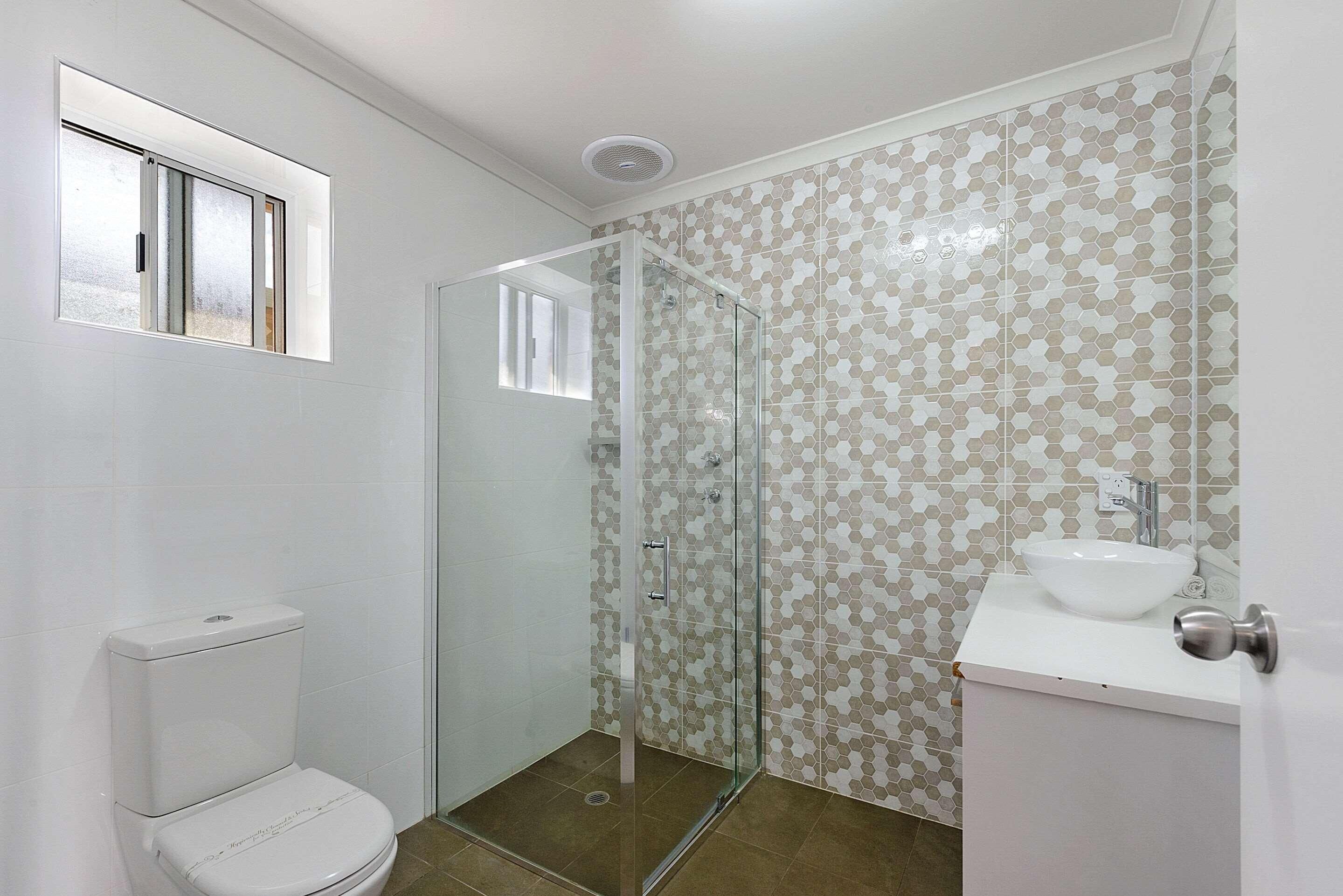 A bathroom with a toilet, a glass-enclosed shower, and a sink with a mirror.