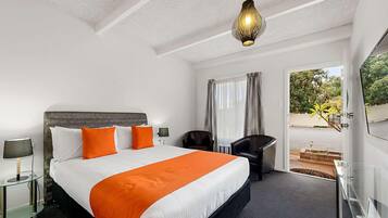 A hotel room with a large bed, a desk, a chair, a TV, and a view of the outdoors.