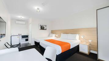 A hotel room with two beds, a desk, a chair, a microwave, and a nightstand with a lamp.