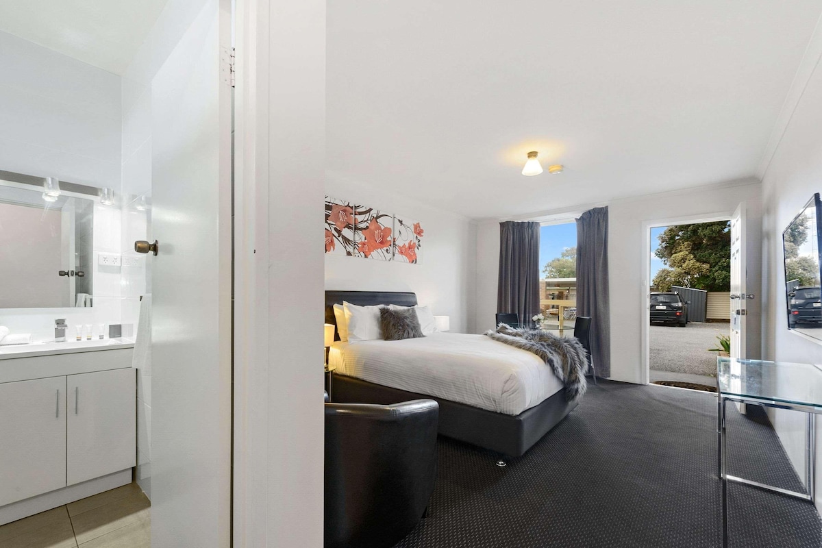 A modern hotel room with a bed, bedside table, and a view of the outside.