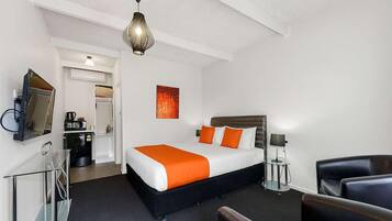 A hotel room with a bed, a desk with a computer, a chair, a lamp, and a ceiling light.