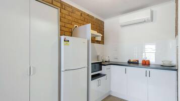 A kitchen with white cabinets, a refrigerator, a microwave, and a brick wall.