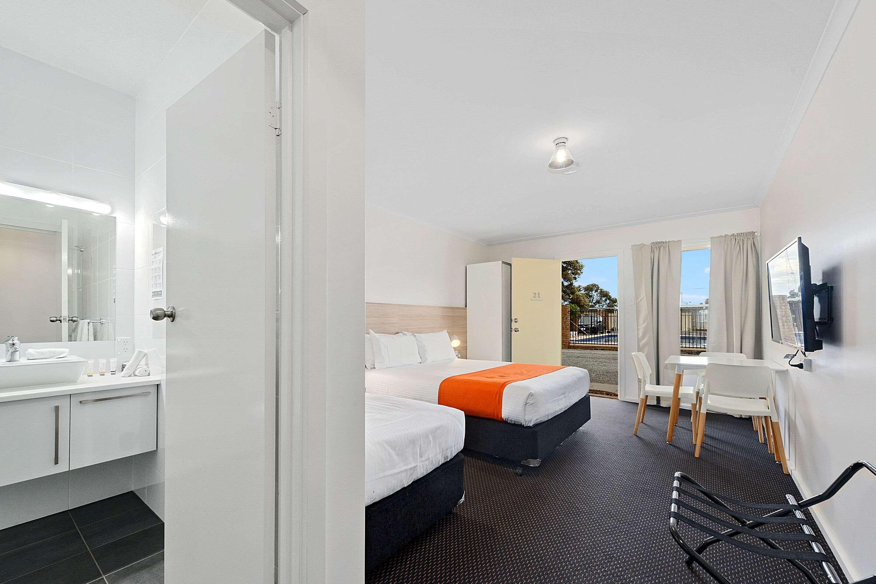 A hotel room with a bathroom, two beds, a desk, and a TV.