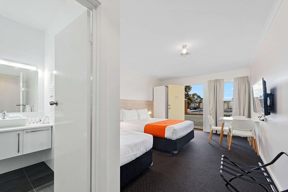 A hotel room with a bathroom, two beds, a desk, and a TV.