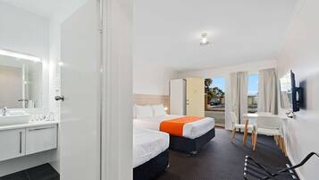 A hotel room with a bathroom, two beds, a desk, and a TV.
