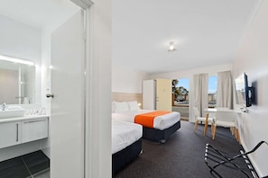 A hotel room with a bathroom, two beds, a desk, and a TV.