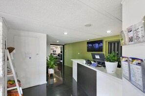 Uma área de recepção com balcão, computador, planta em vaso e cartazes informativos.