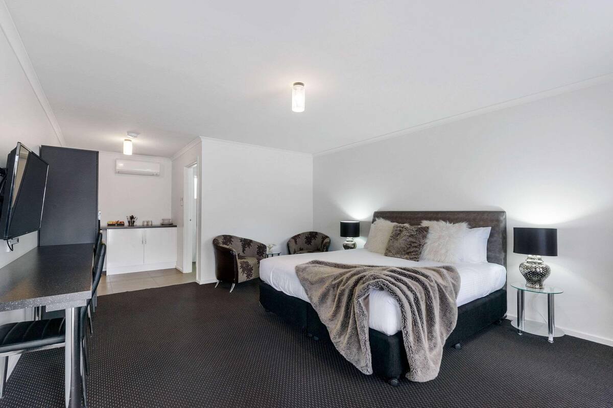 Habitación de hotel con cama, escritorio, silla, mesita, lámpara y aire acondicionado instalado en la pared.