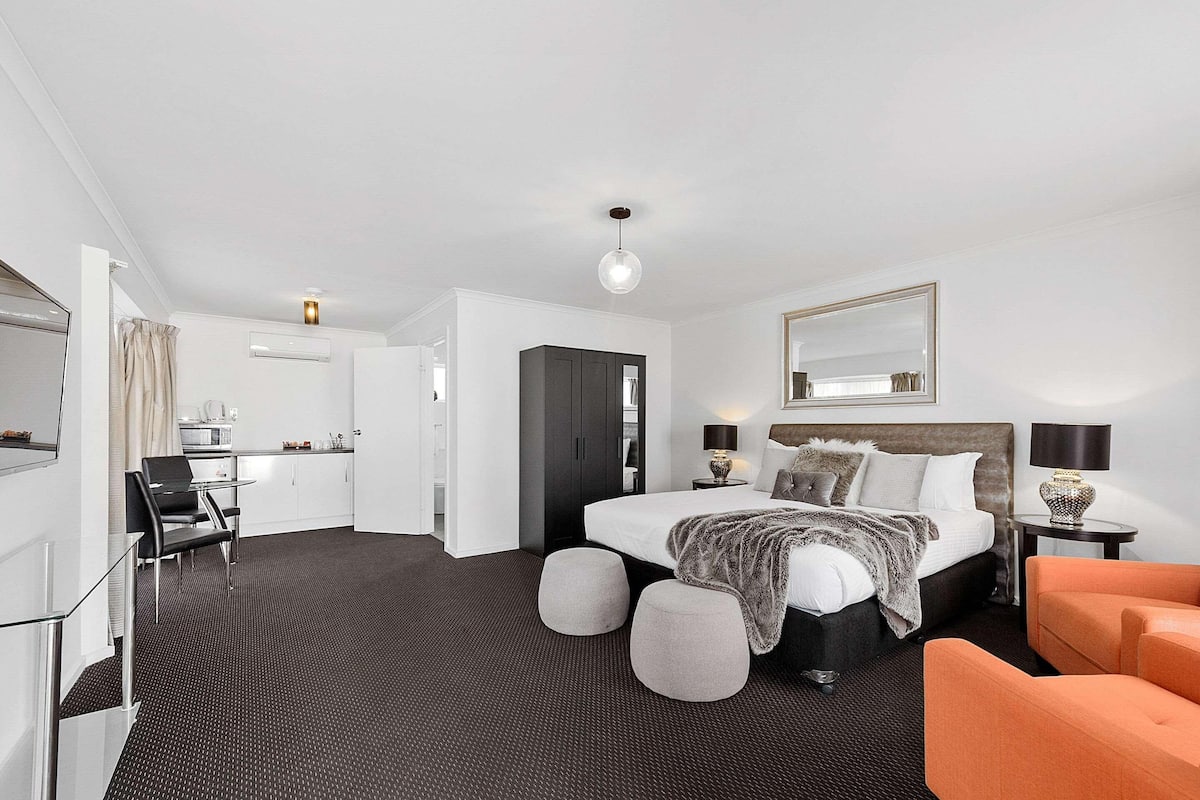 A modern hotel room with a bed, bedside tables, a desk, and a chair.
