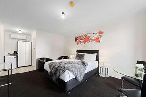 A hotel room with a bed, bedside tables, a desk, a chair, a small table with a vase, and a wall-mounted artwork.