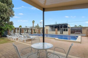 A covered outdoor pool area with lounge chairs and a table, a clear blue sky, and a building in the background. - Comfort Inn Flinders On Main (Beetaloo Valley)