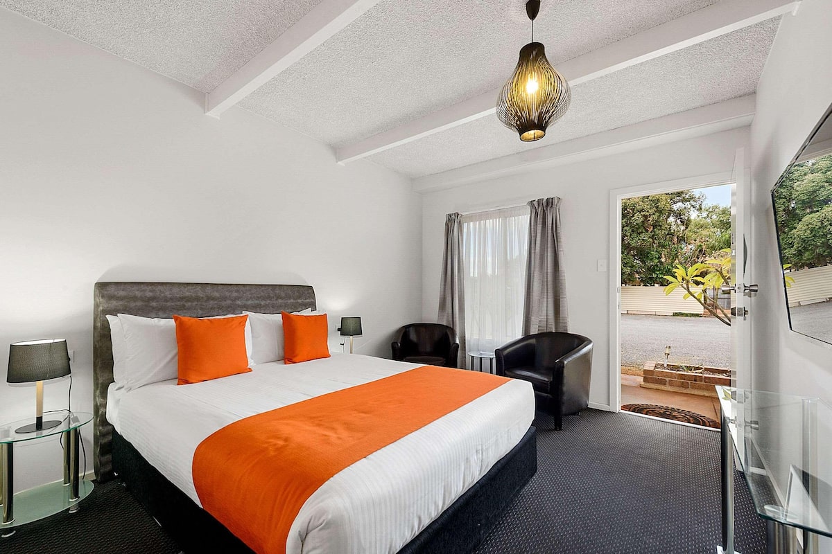 Habitación de hotel con una cama grande, un escritorio, una silla, un televisor y vistas al exterior.