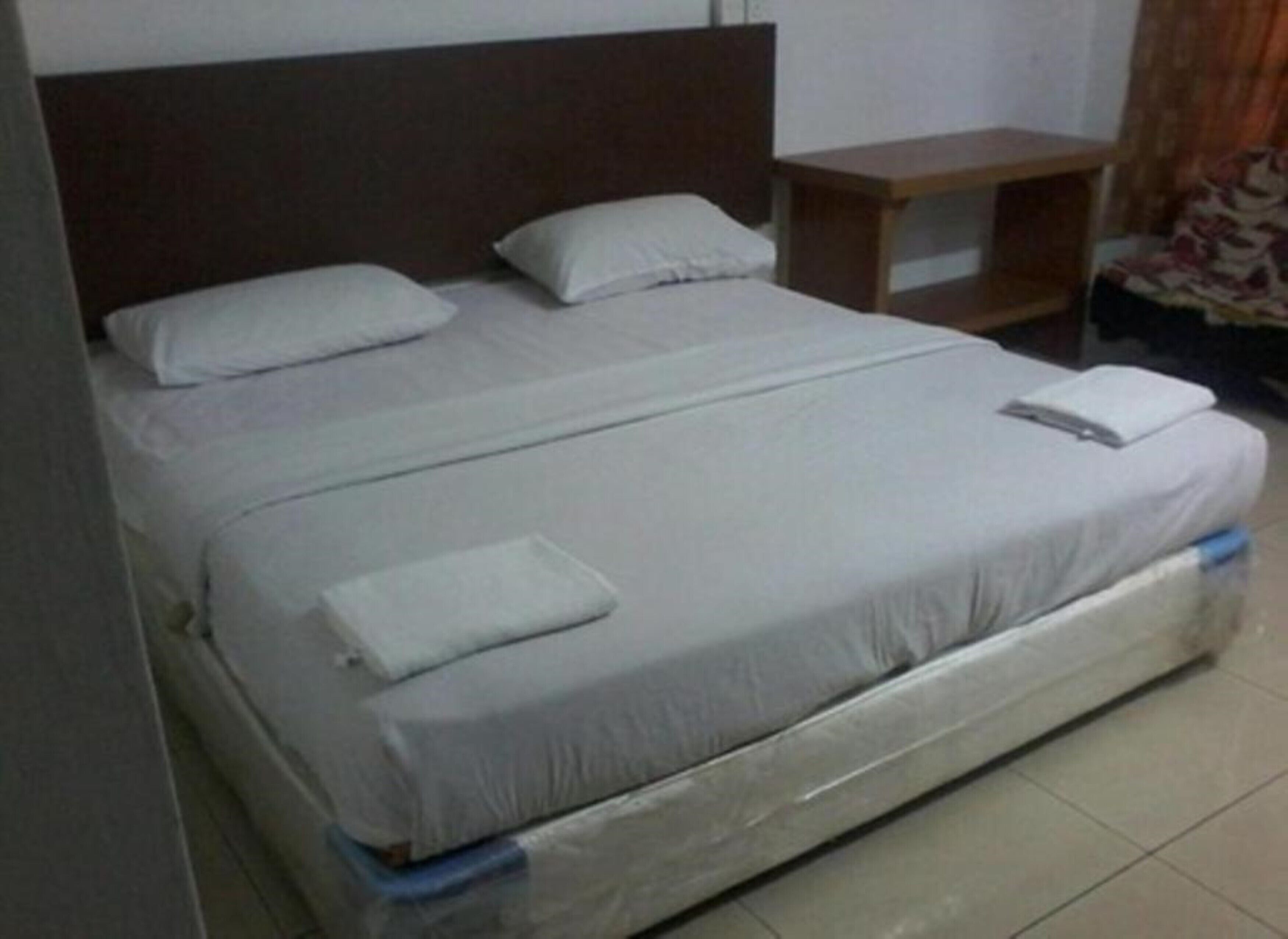 A single bed with white bedding, a wooden headboard, a small wooden nightstand, and a tiled floor.