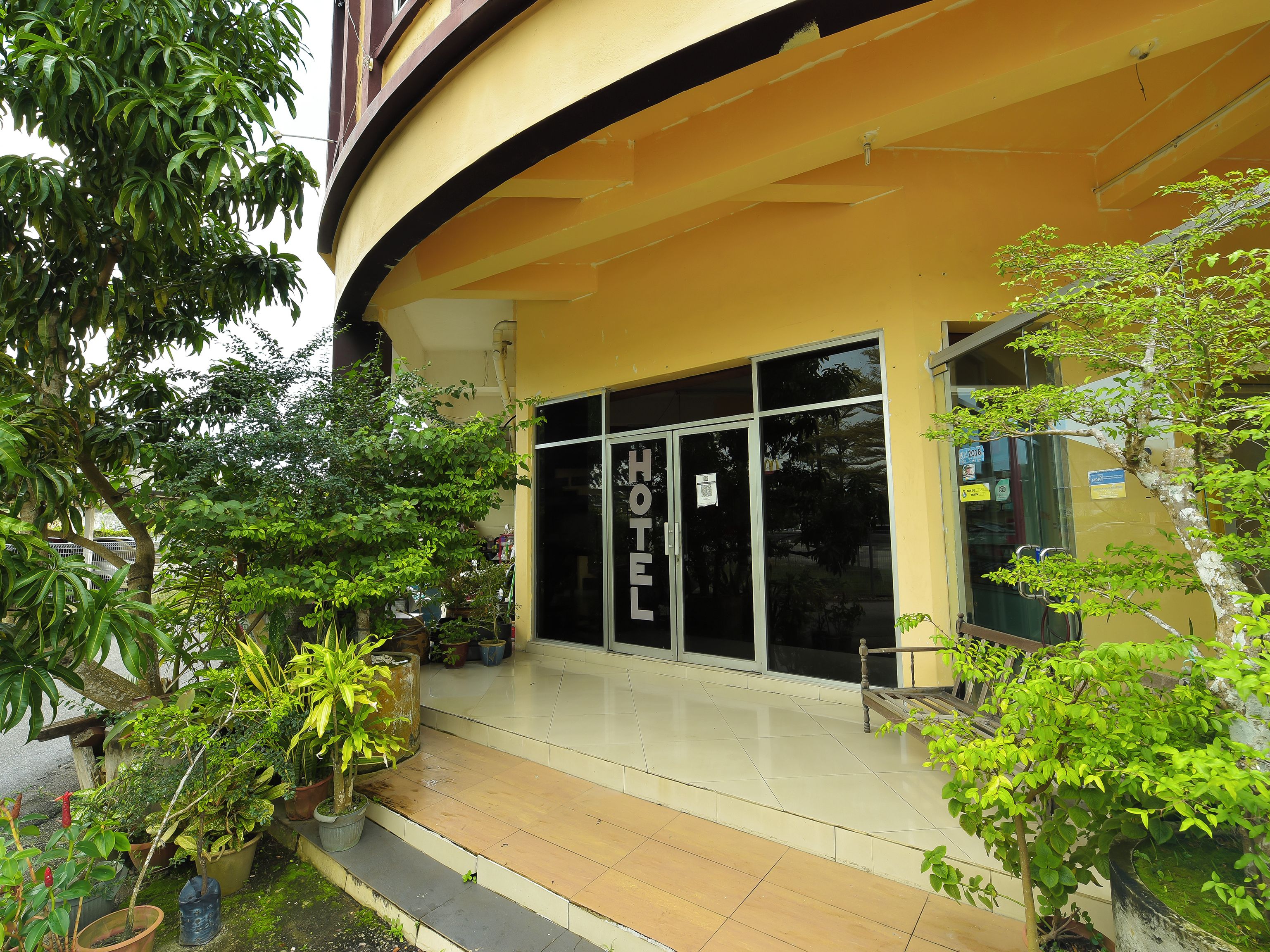 A hotel entrance with a glass door, potted plants, and a tiled walkway.