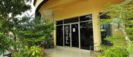 A hotel entrance with a glass door, potted plants, and a tiled walkway.
