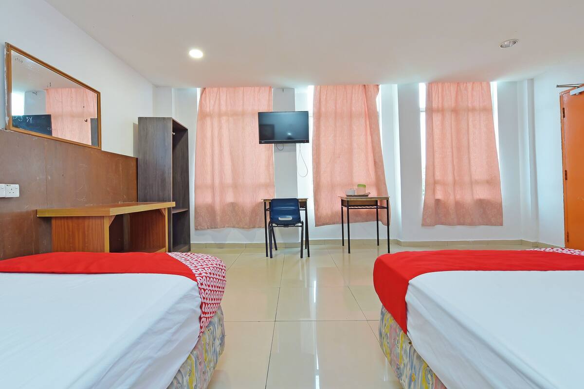 Una habitación de hotel con dos camas, un escritorio, una silla, un televisor y un armario.