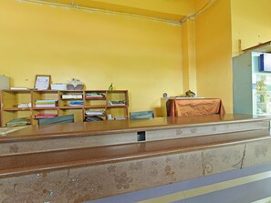A reception desk with a brown marble top, wooden shelving with various items, and a yellow wall.