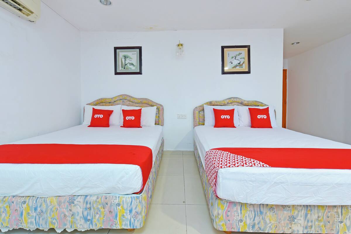 Habitación de hotel con dos camas, cada una con colcha y almohadas rojas y blancas.