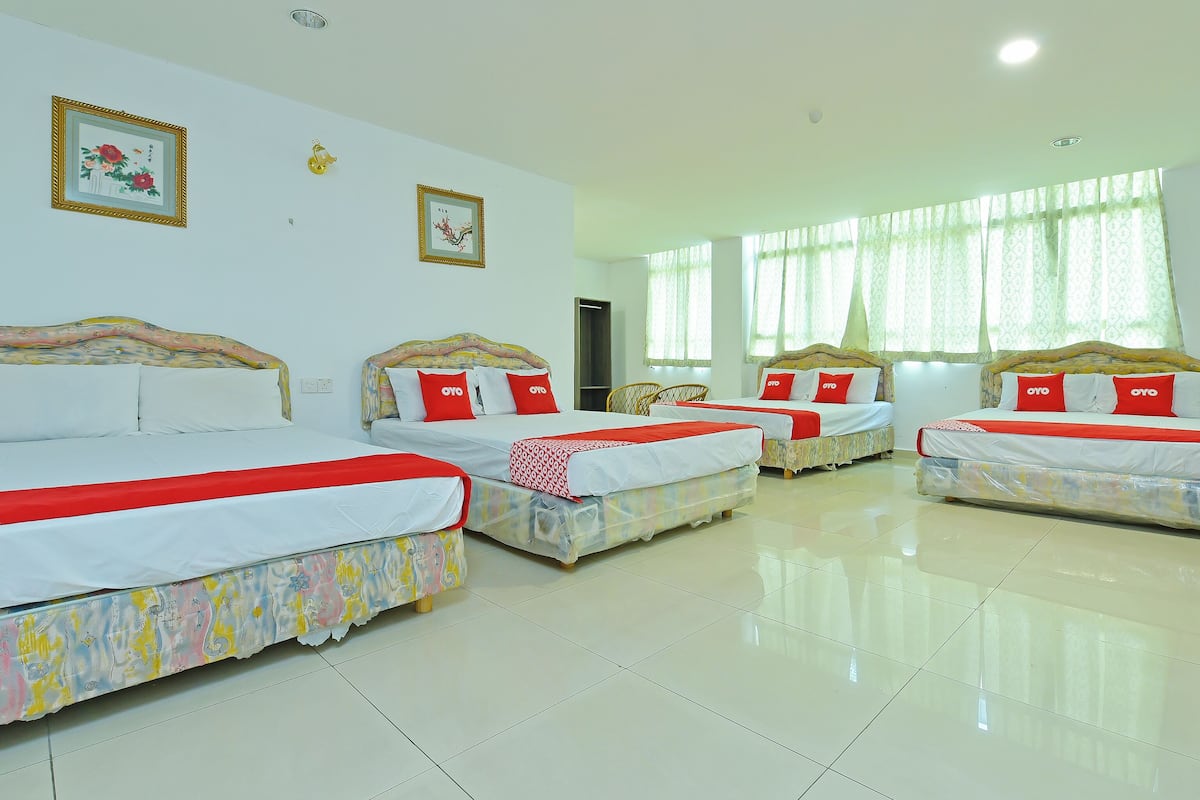 A hotel room with four beds, each with a red and white bedspread, and a large window with sheer curtains.