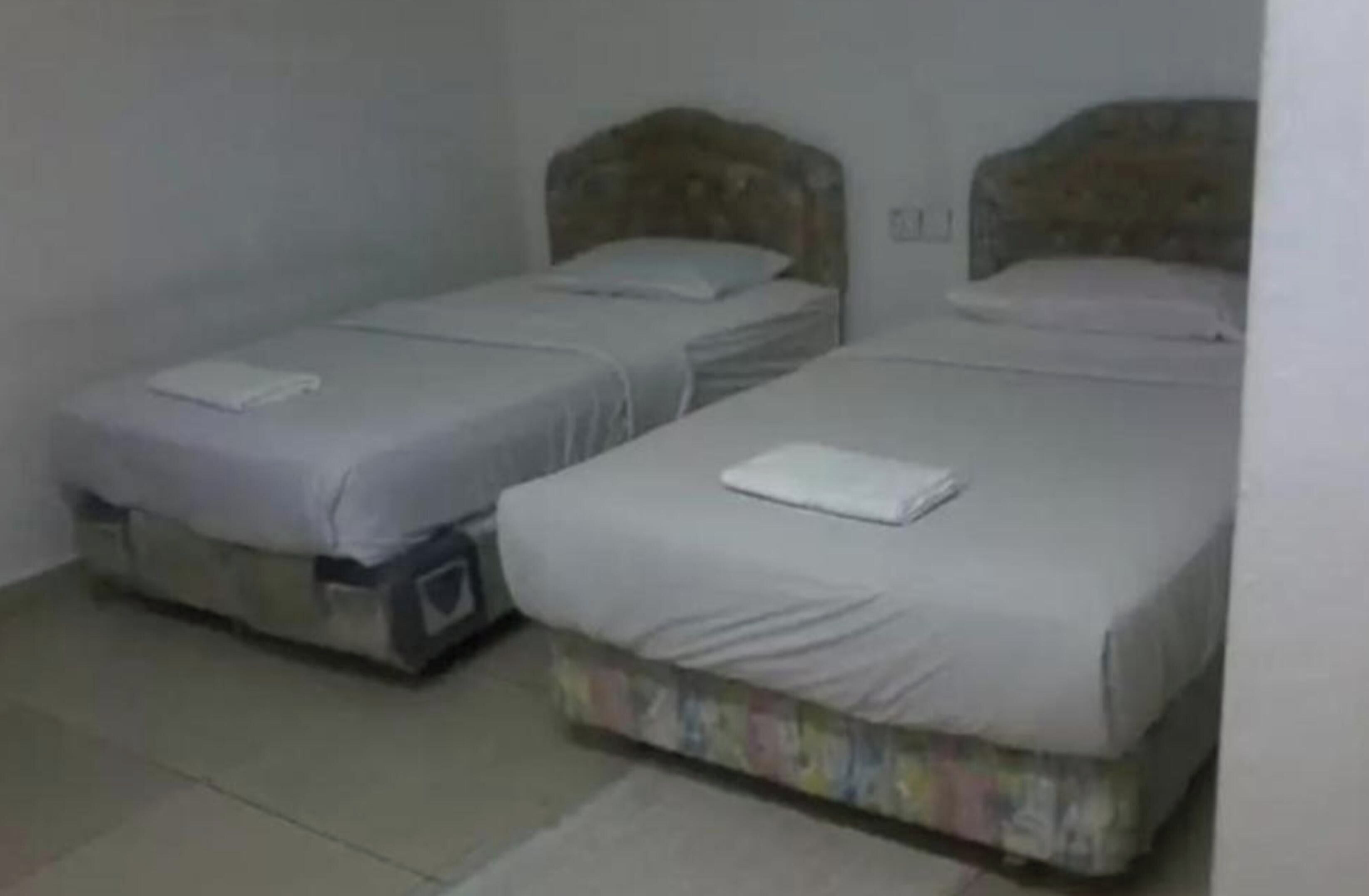 Two single beds with headboards, a small bedside table, and a wall-mounted light fixture.