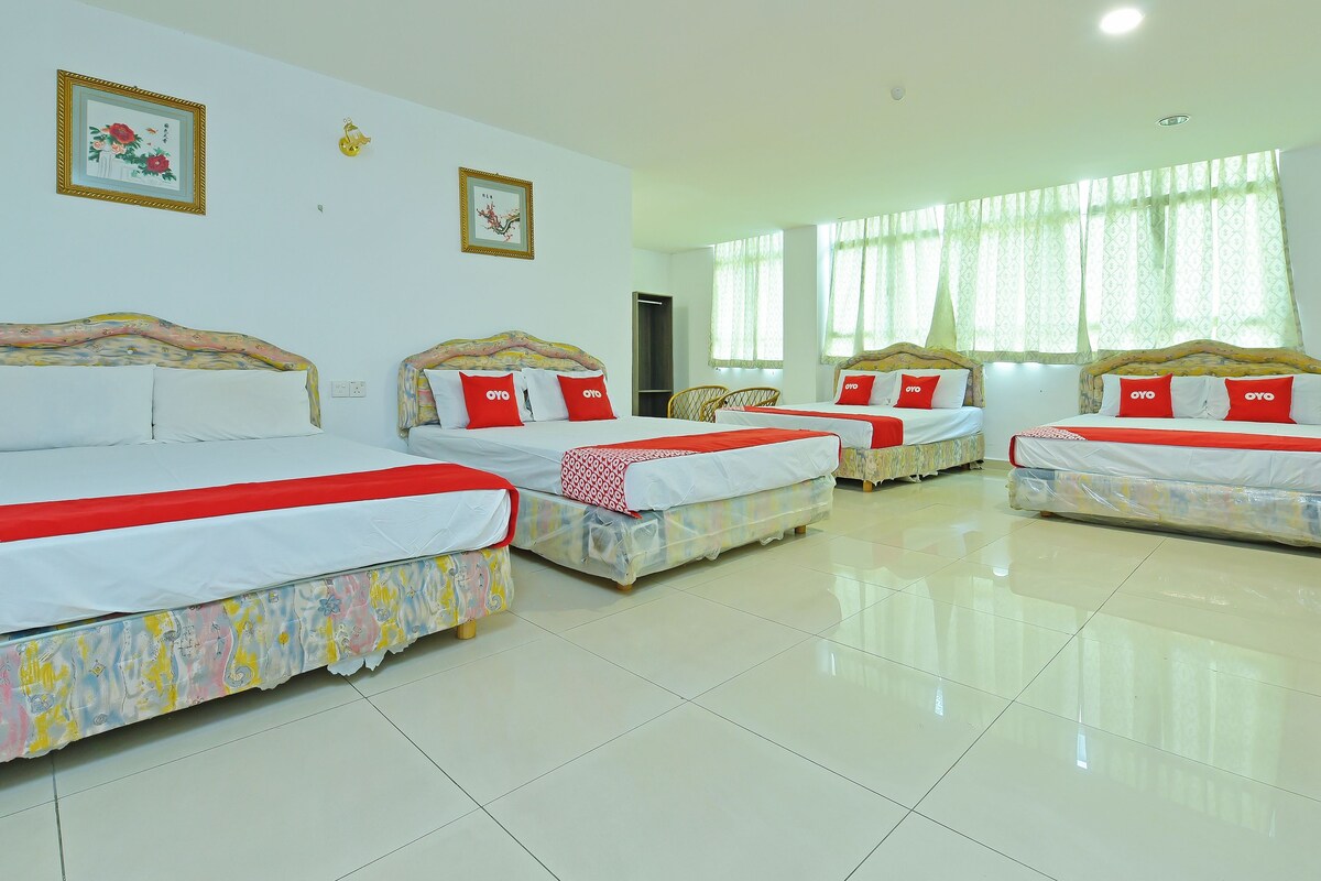 Habitación de hotel con cuatro camas, cada una con cubrecama rojo y blanco, y un ventanal con cortinas translúcidas.