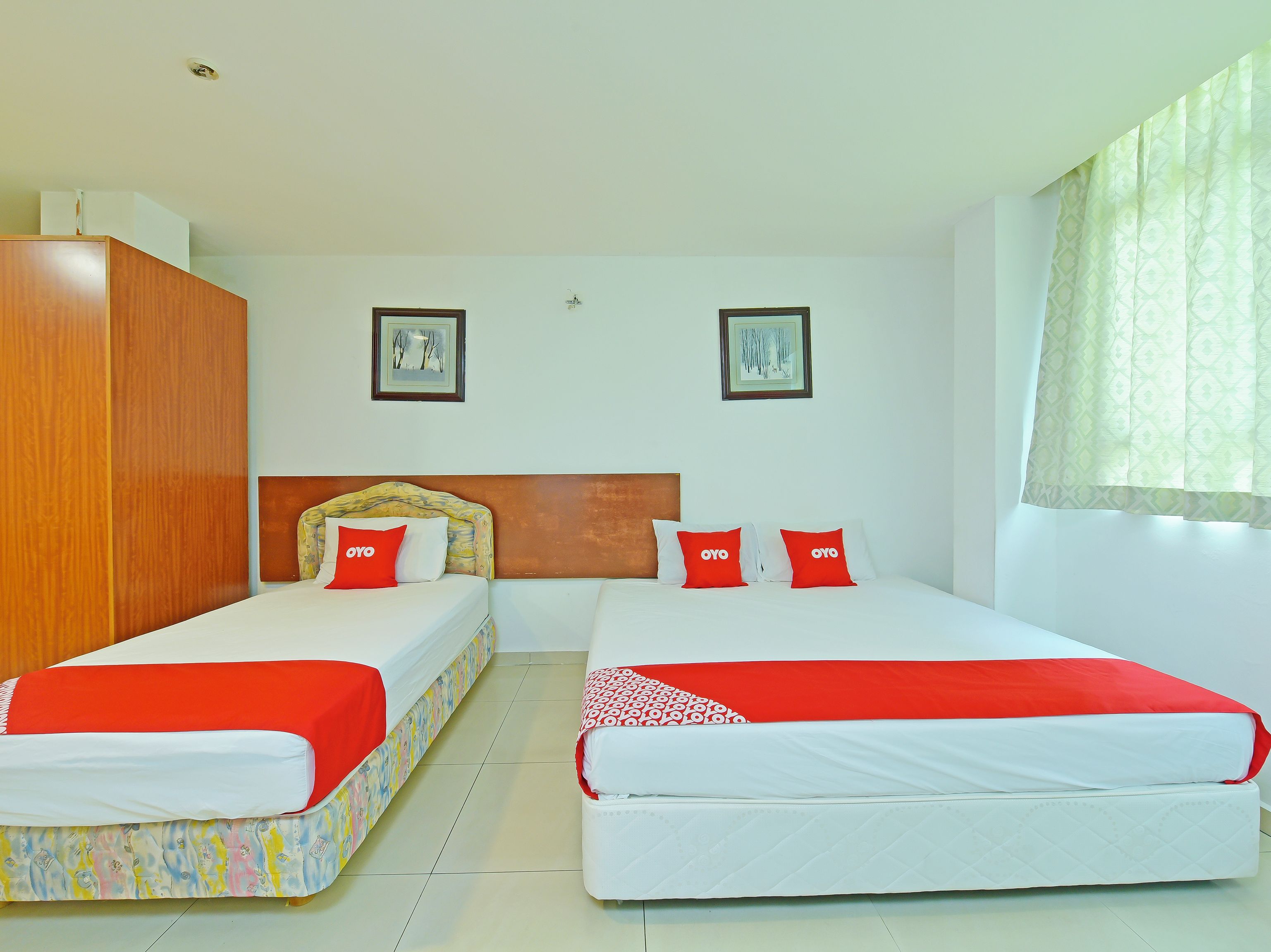 A hotel room with two beds, each with a red and white bedspread, and a wooden wardrobe.