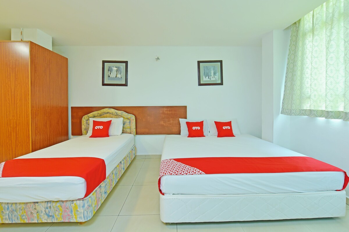 A hotel room with two beds, each with a red and white bedspread, and a wooden wardrobe.