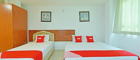 A hotel room with two beds, each with a red and white bedspread, and a wooden wardrobe.