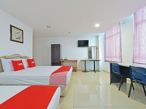 A hotel room with two beds, a desk, a chair, a TV, and a door.