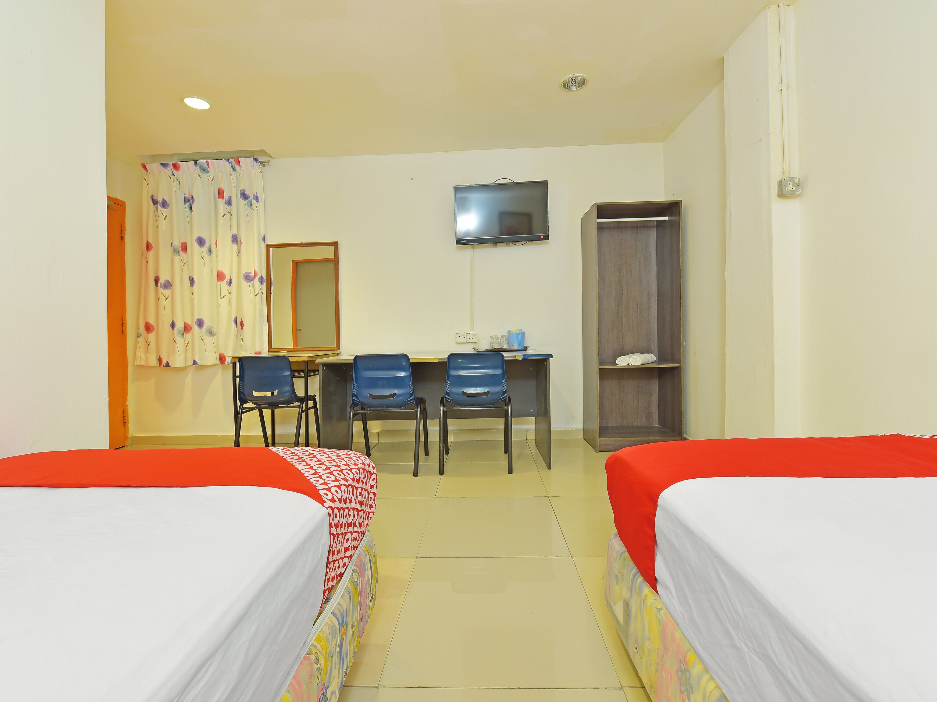A hotel room with two single beds, a desk with chairs, a TV, and a wardrobe.