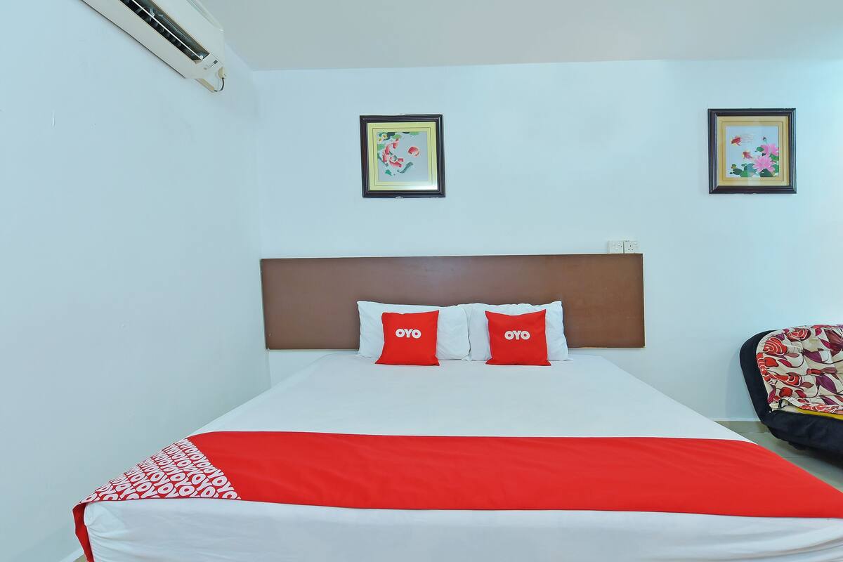 Habitación de hotel con cama, dos almohadas con el nombre de marca 'OYO', una colcha roja y blanca, y dos cuadros enmarcados en la pared.