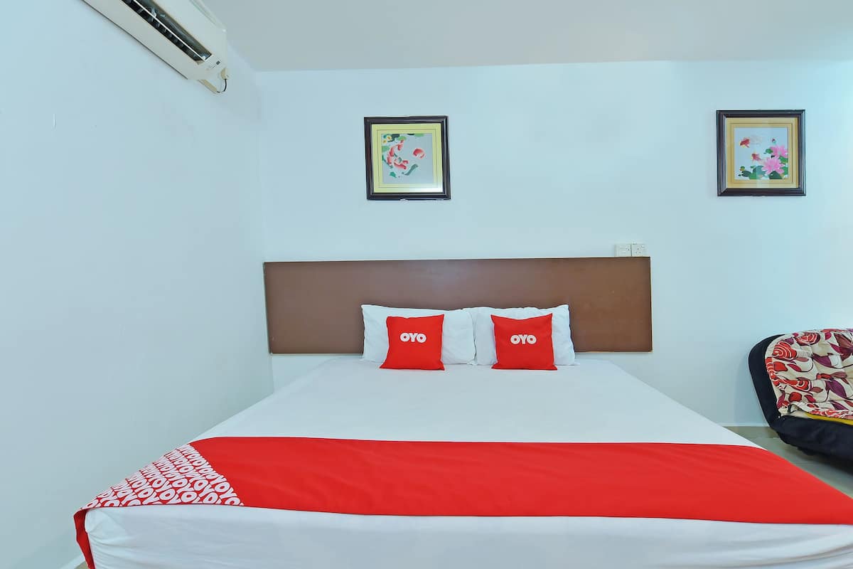 A hotel room with a bed, two pillows with the brand name 'OYO', a red and white blanket, and two framed pictures on the wall.