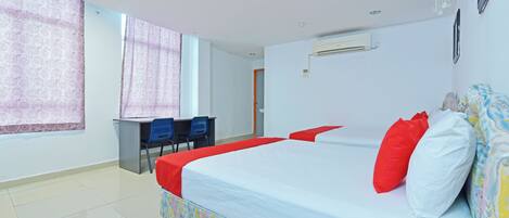 A hotel room with a large bed, a desk with two chairs, and a window with patterned curtains.