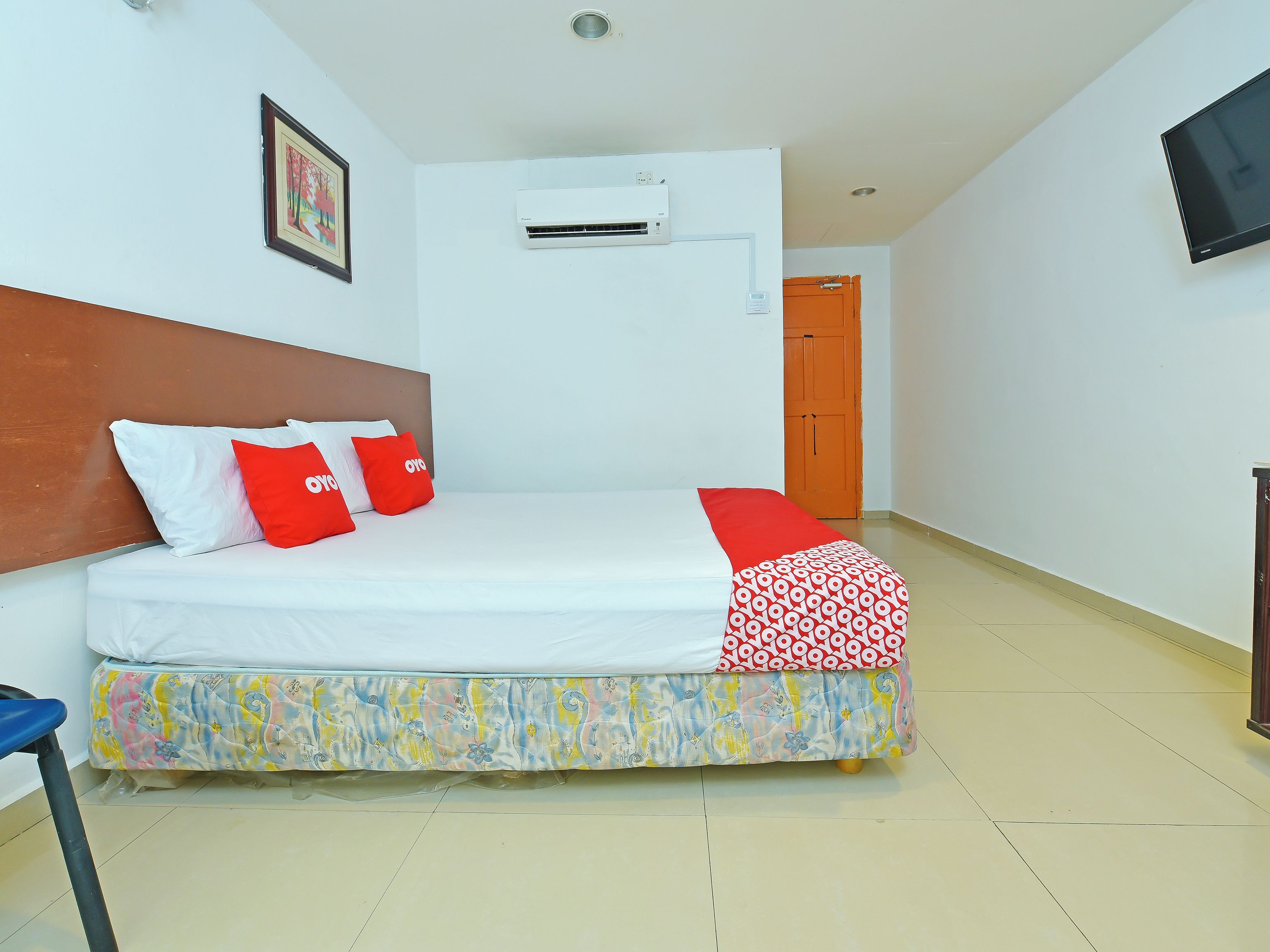 A neatly made bed with white and red bedding, a wooden headboard, and a colorful bed skirt.