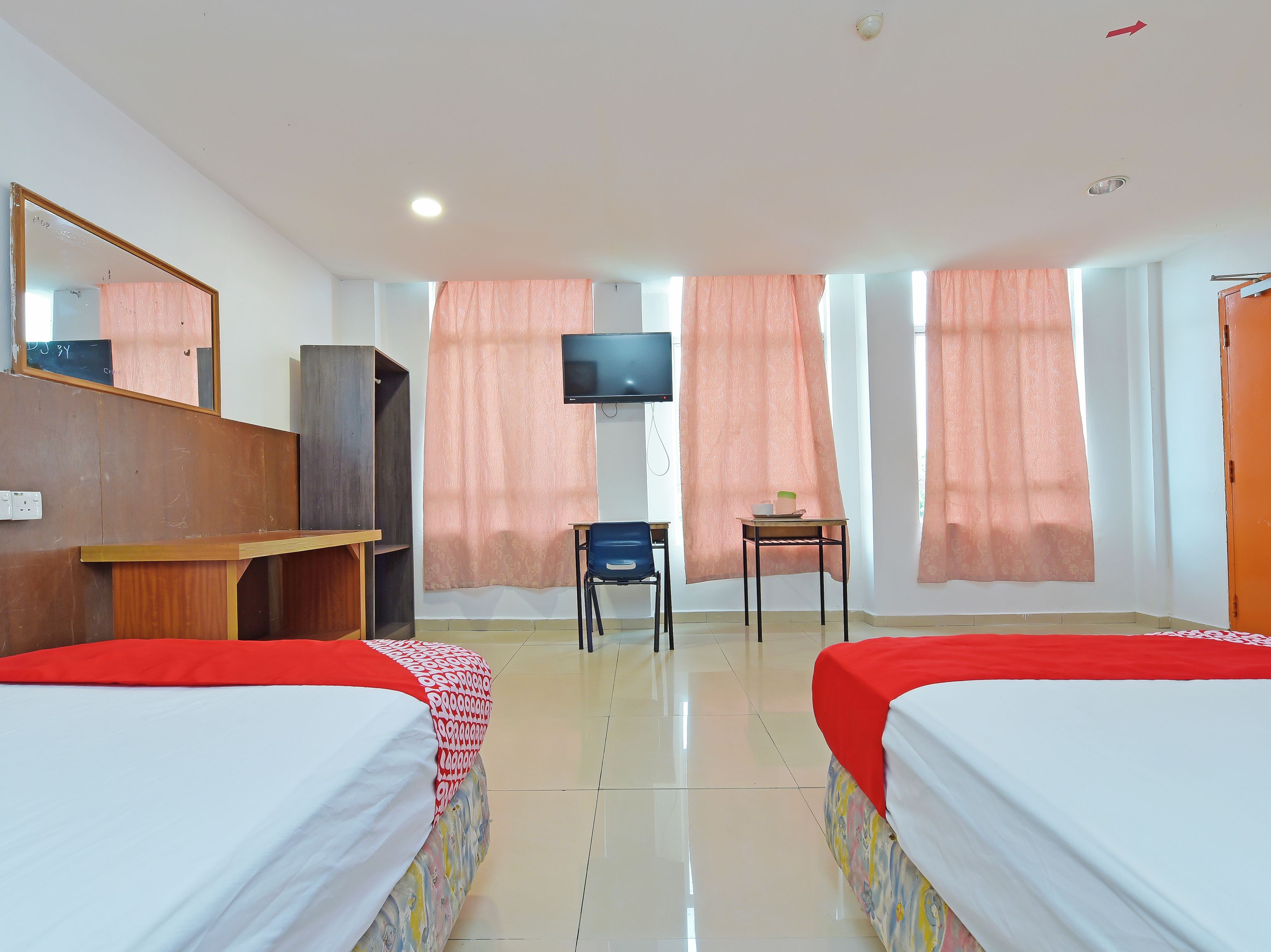 A hotel room with two beds, a desk, a chair, a television, and a wardrobe.