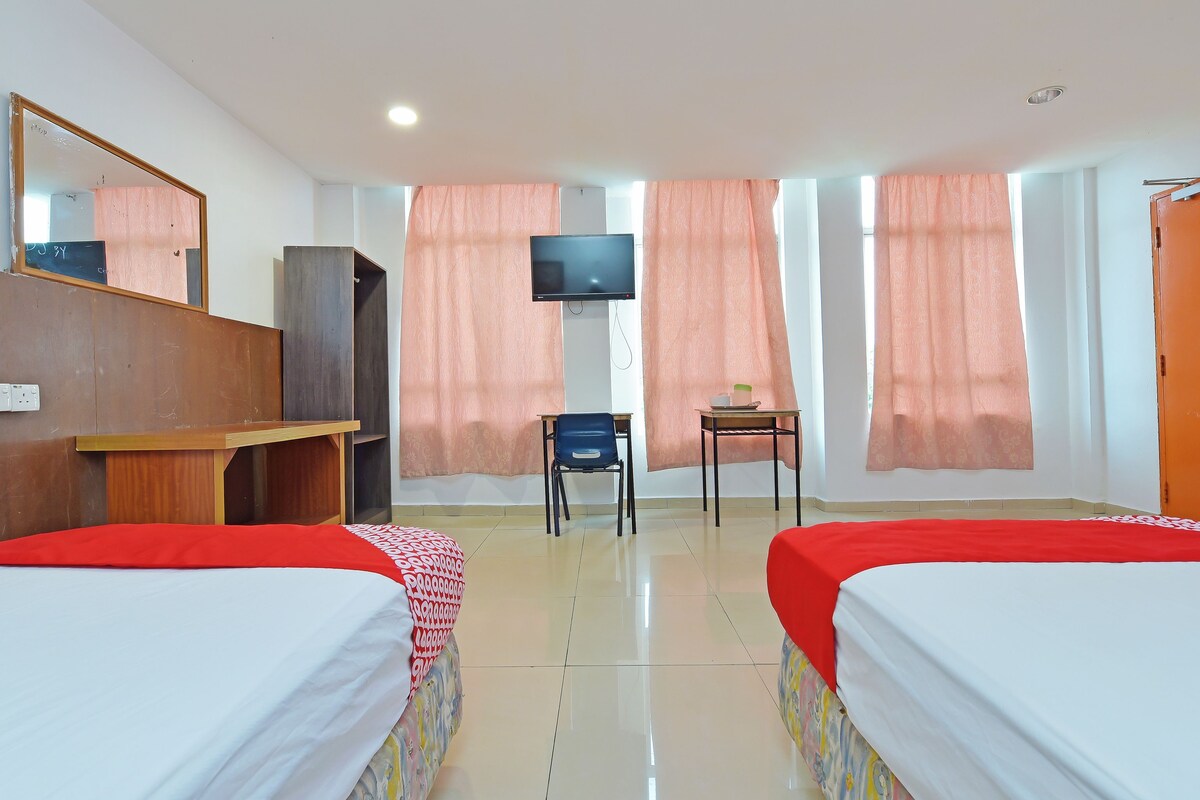 A hotel room with two beds, a desk, a chair, a television, and a wardrobe.