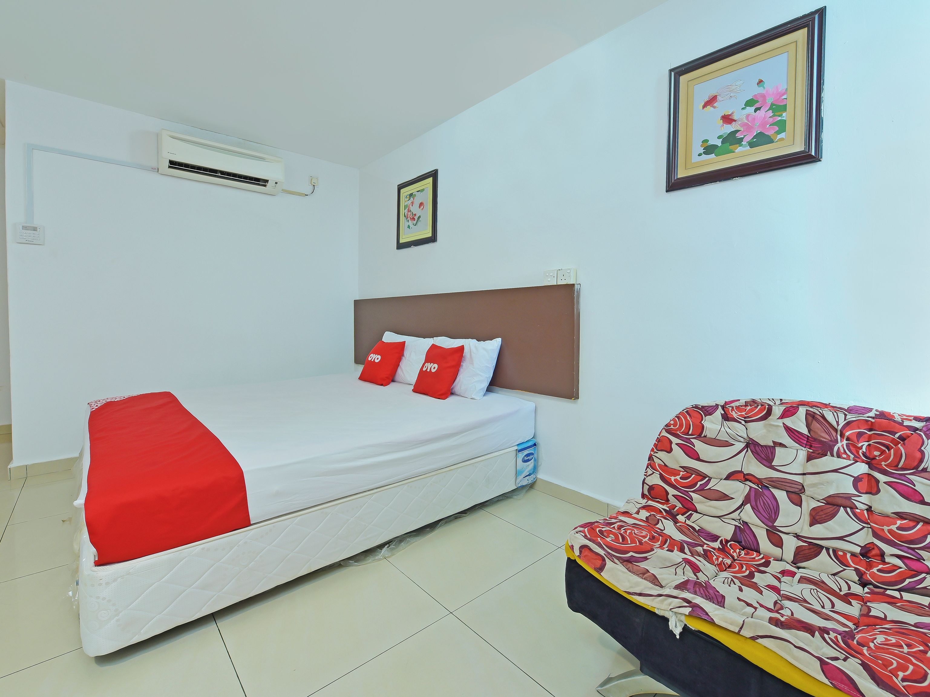 Habitación de hotel con cama, sillón, aire acondicionado y un cuadro en la pared.
