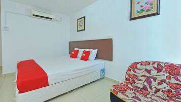 Habitación de hotel con cama, sillón, aire acondicionado y un cuadro en la pared.
