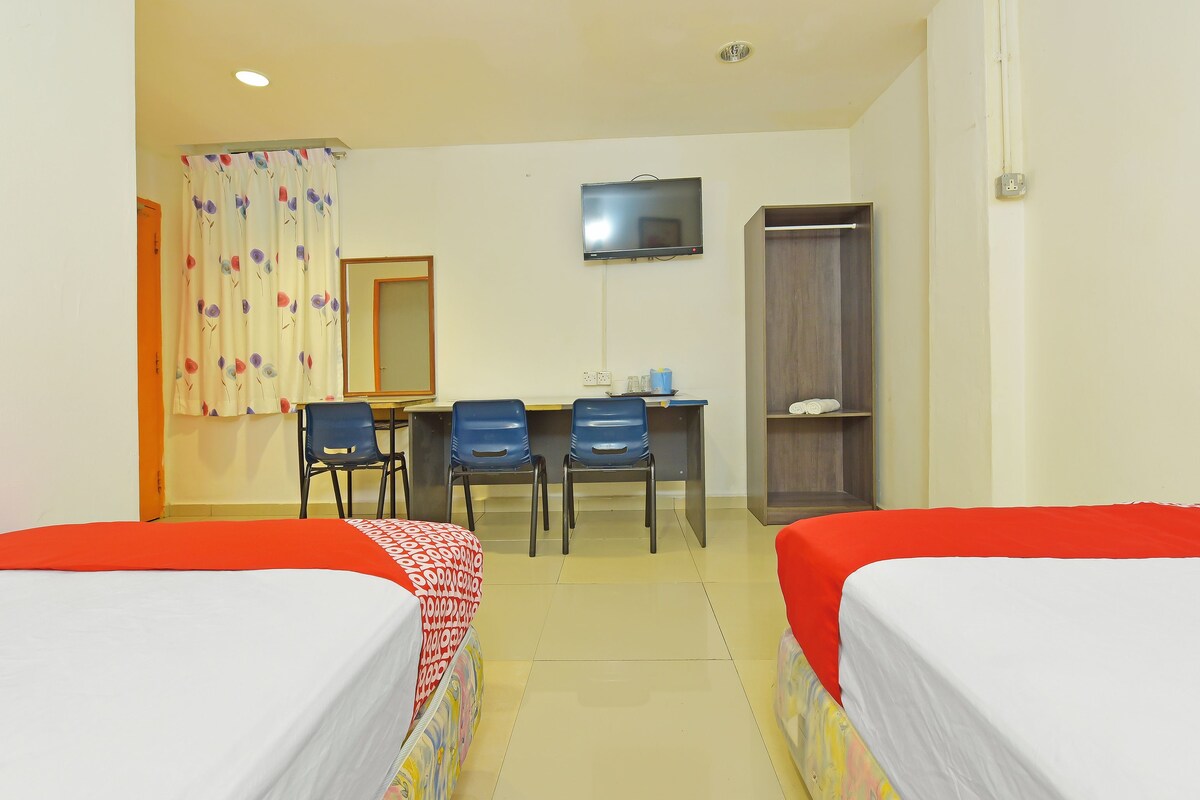 A hotel room with two single beds, a desk with chairs, a TV, and a wardrobe.