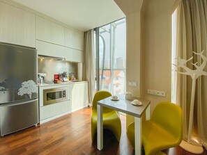 A compact kitchen with a refrigerator, oven, and sink, a dining table with chairs, and a large window offering a view. - ST Residences Novena (Singapore)